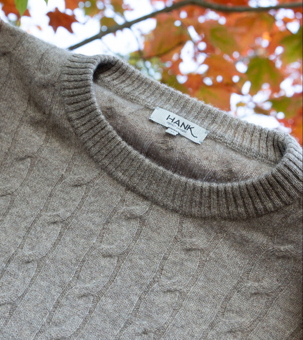 Gray cable knit sweater with 'Hank' label against a blurred autumn background